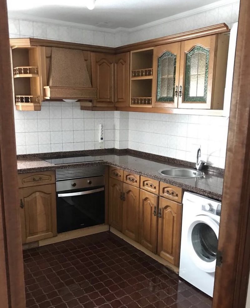 Cocina vista desde la puerta antes del home staging: muebles de madera oscura y suelo marrón