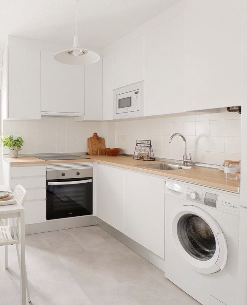 Cocina vista desde la puerta después del home staging: muebles esmaltados en blanco, encimera de madera y suelo claro