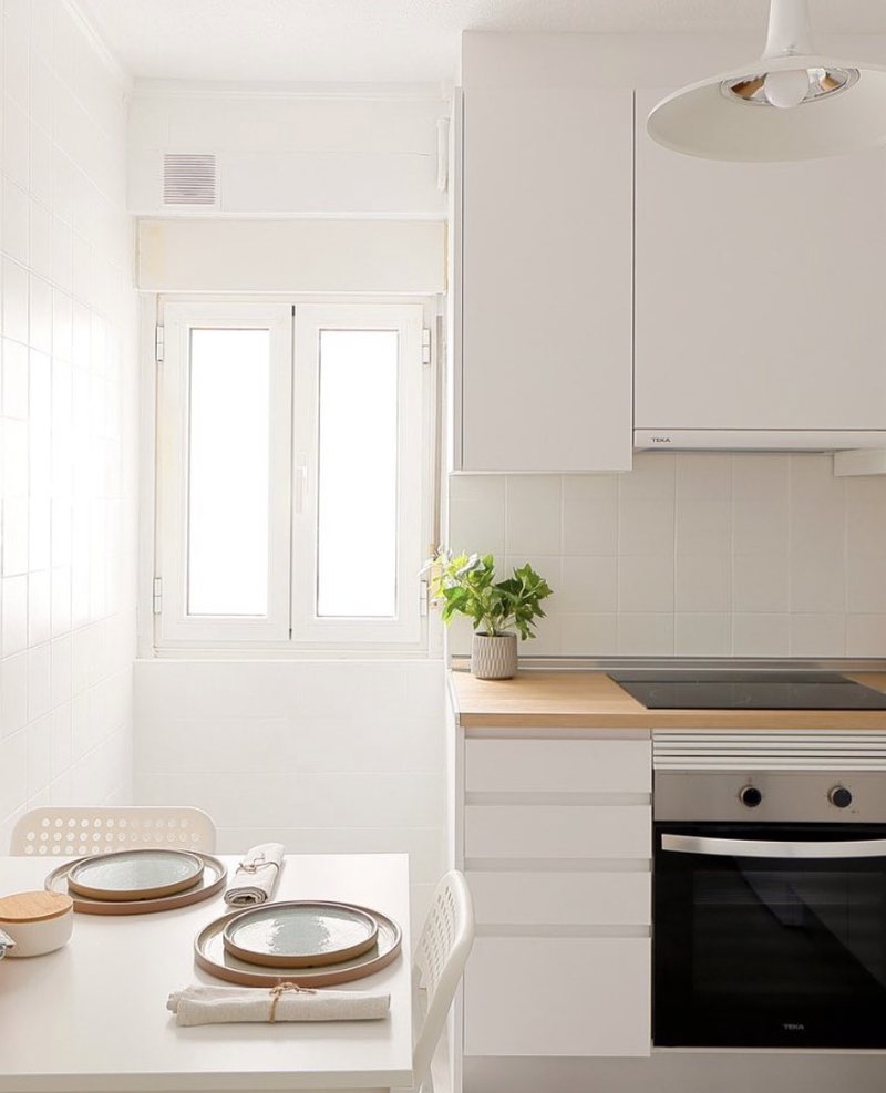 Cocina vista hacia la ventana después del home staging: muebles esmaltados en blanco, encimera de madera y suelo claro